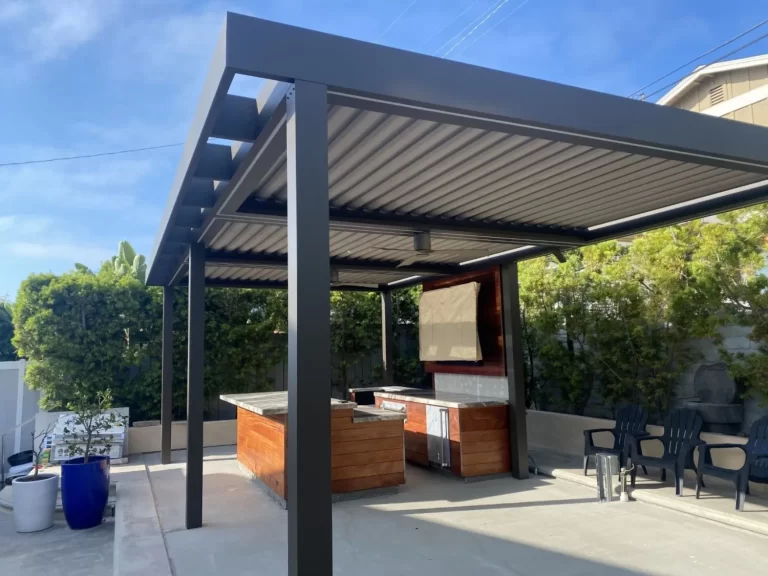 Black aluminum pergola structure housing a built-in outdoor kitchen with TV display