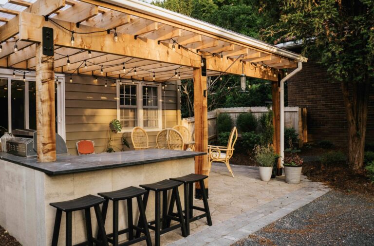 Covered outdoor kitchen and entertaining area featuring a built-in bar, grill, wood ceiling, and comfortable dining space.