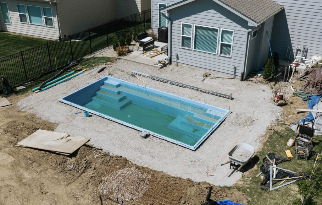 Aerial view of newly installed rectangular fiberglass pool surrounded by raw soil site