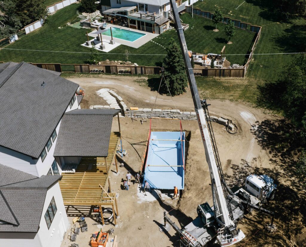 Drone shot of crane lifting pool shell over house for backyard pool installation