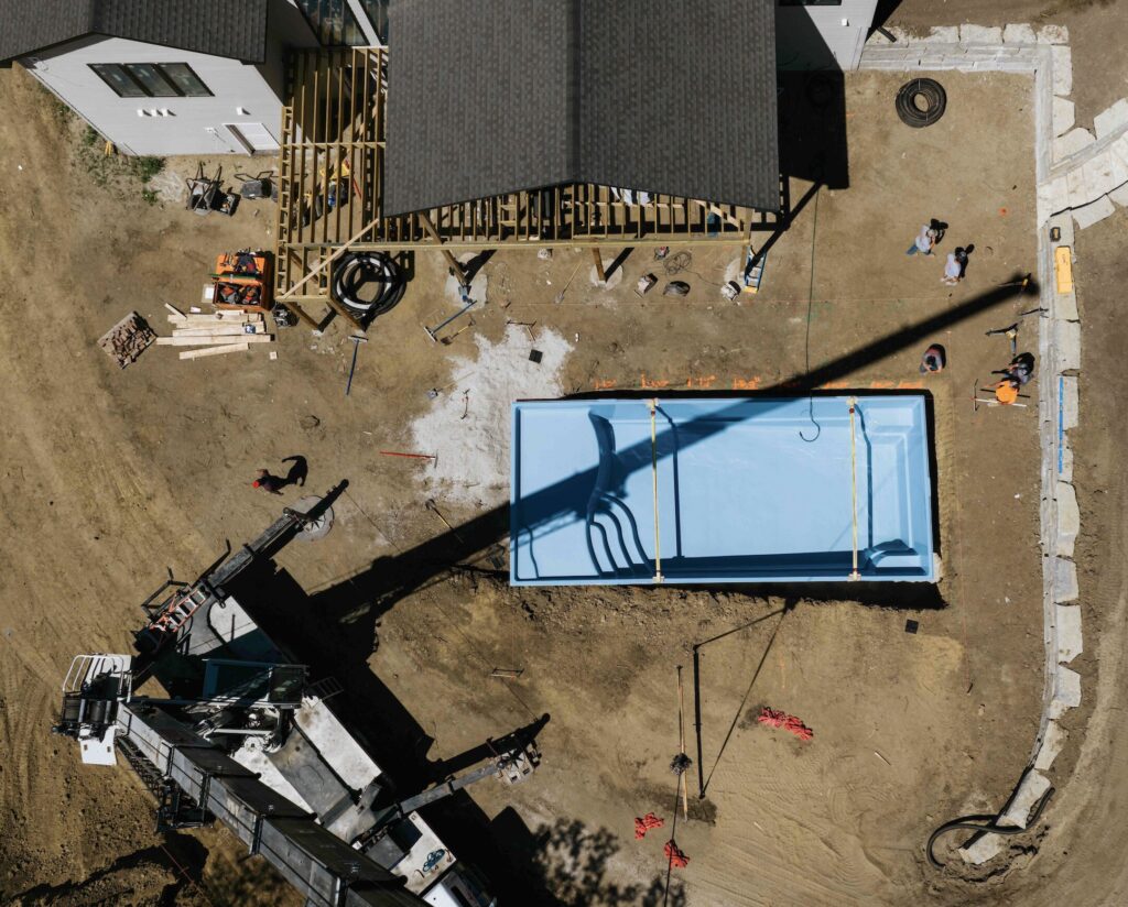 Aerial view of pool installation site with crane placing fiberglass pool shell into ground