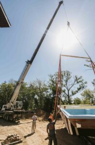 Crane boom lifting pool equipment into backyard during construction project