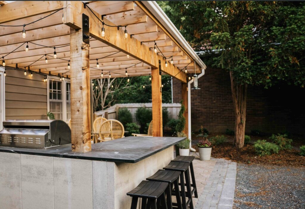 Custom wood pergola with string bistro lighting, patio seating, and built-in outdoor kitchen island