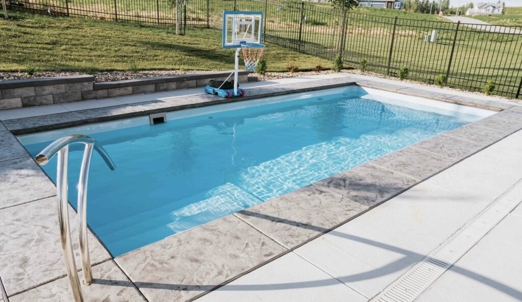 Rectangular inground fiberglass pool filled with clear water set in custom paver patio