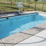 Rectangular inground fiberglass pool filled with clear water set in custom paver patio