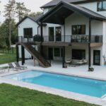 Modern custom home with elevated deck overlooking backyard inground swimming pool