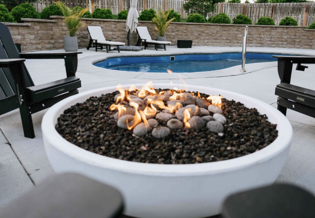 Round gas fire bowl with lava rock set on concrete pool patio deck