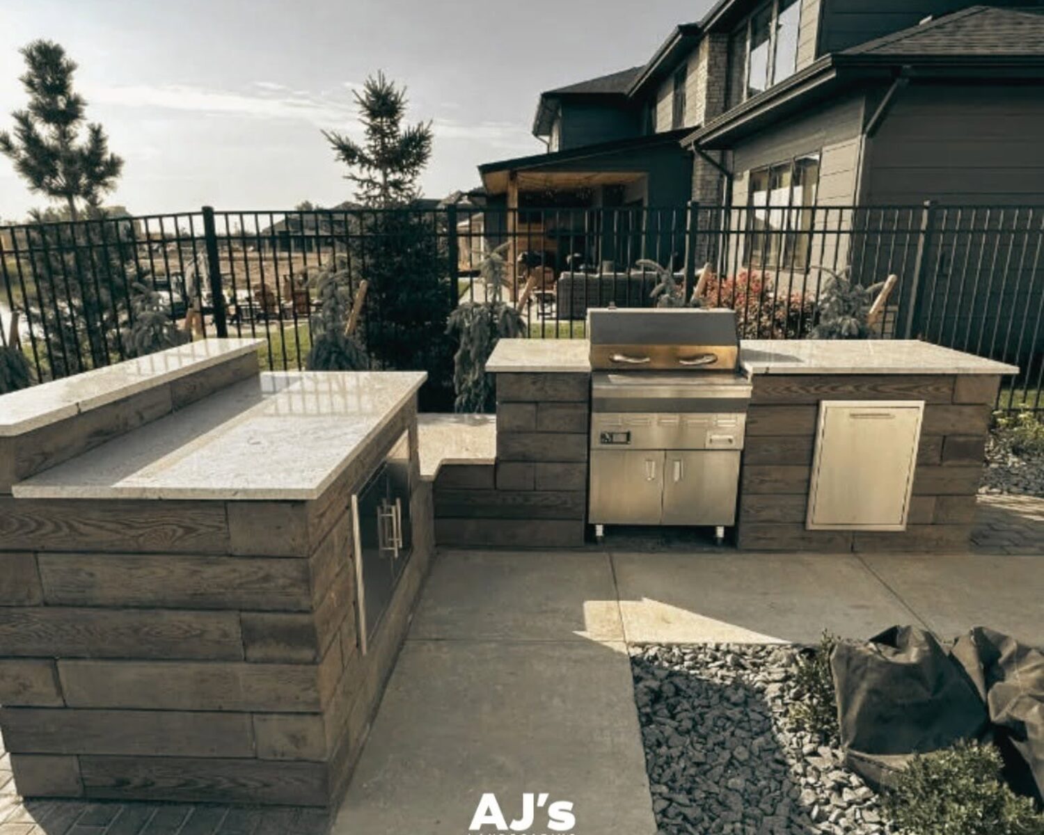 L-shaped outdoor kitchen with bar seating and built-in grill by AJ's Landscaping.