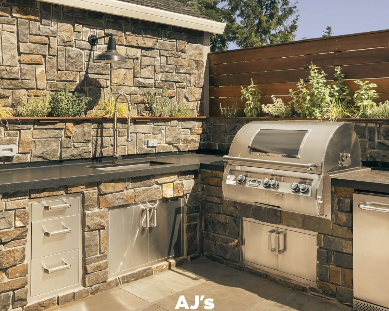 Custom stone outdoor kitchen with built-in stainless steel grill by AJ's Landscaping.