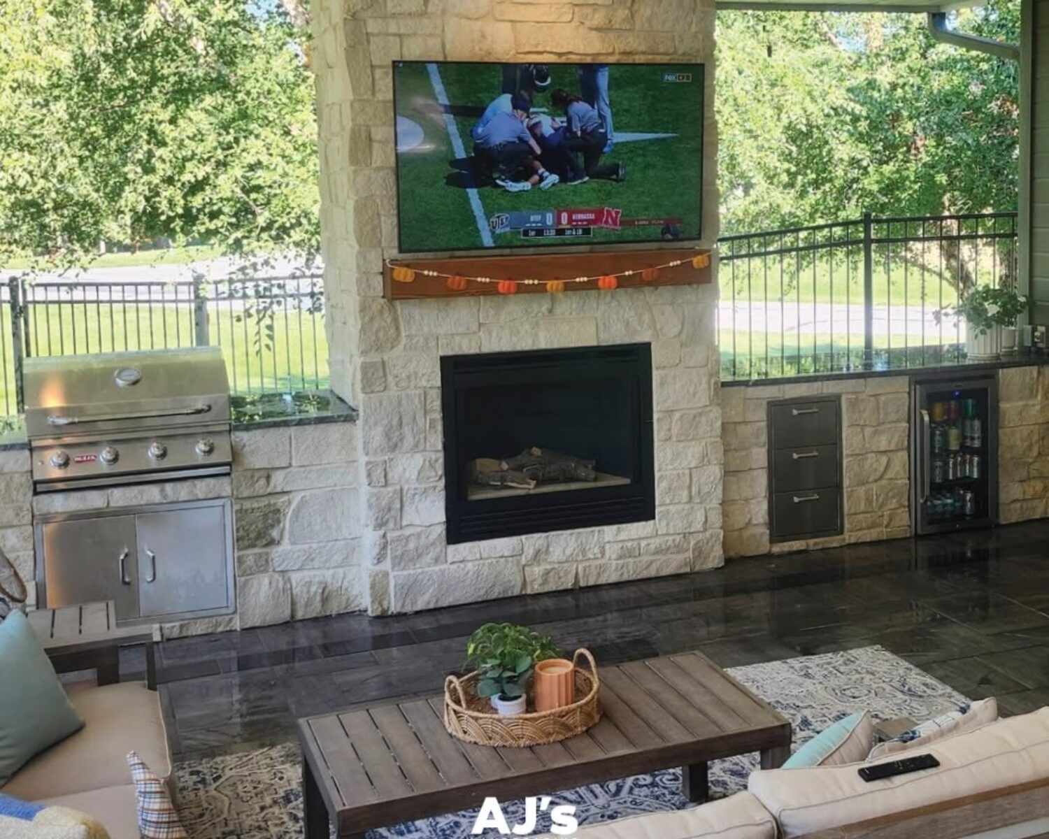 Covered patio featuring a built-in outdoor fireplace and wall-mounted TV by AJ's Landscaping in Omaha.