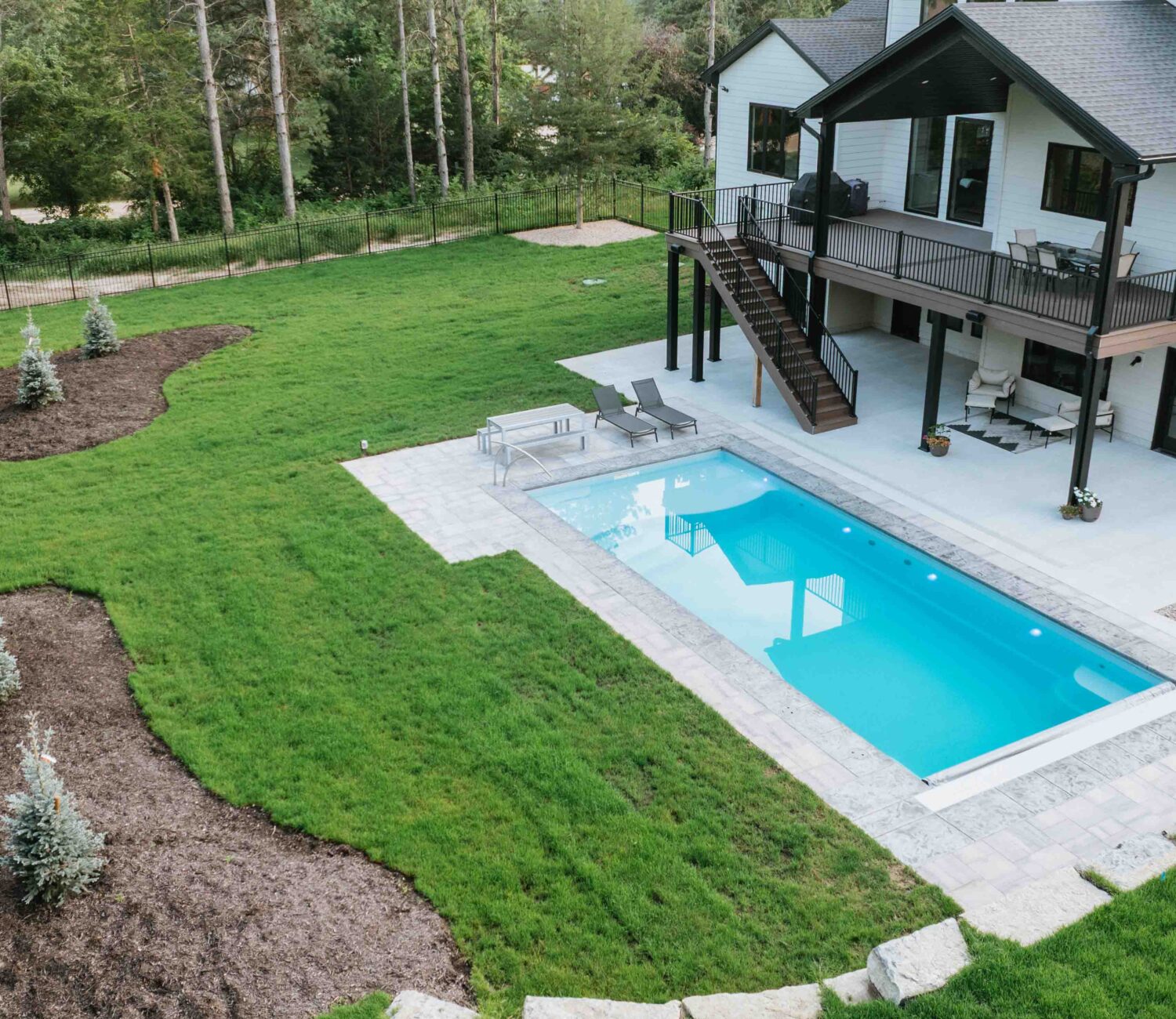 Aerial drone view of rectangular inground swimming pool with green lawn and stone patio