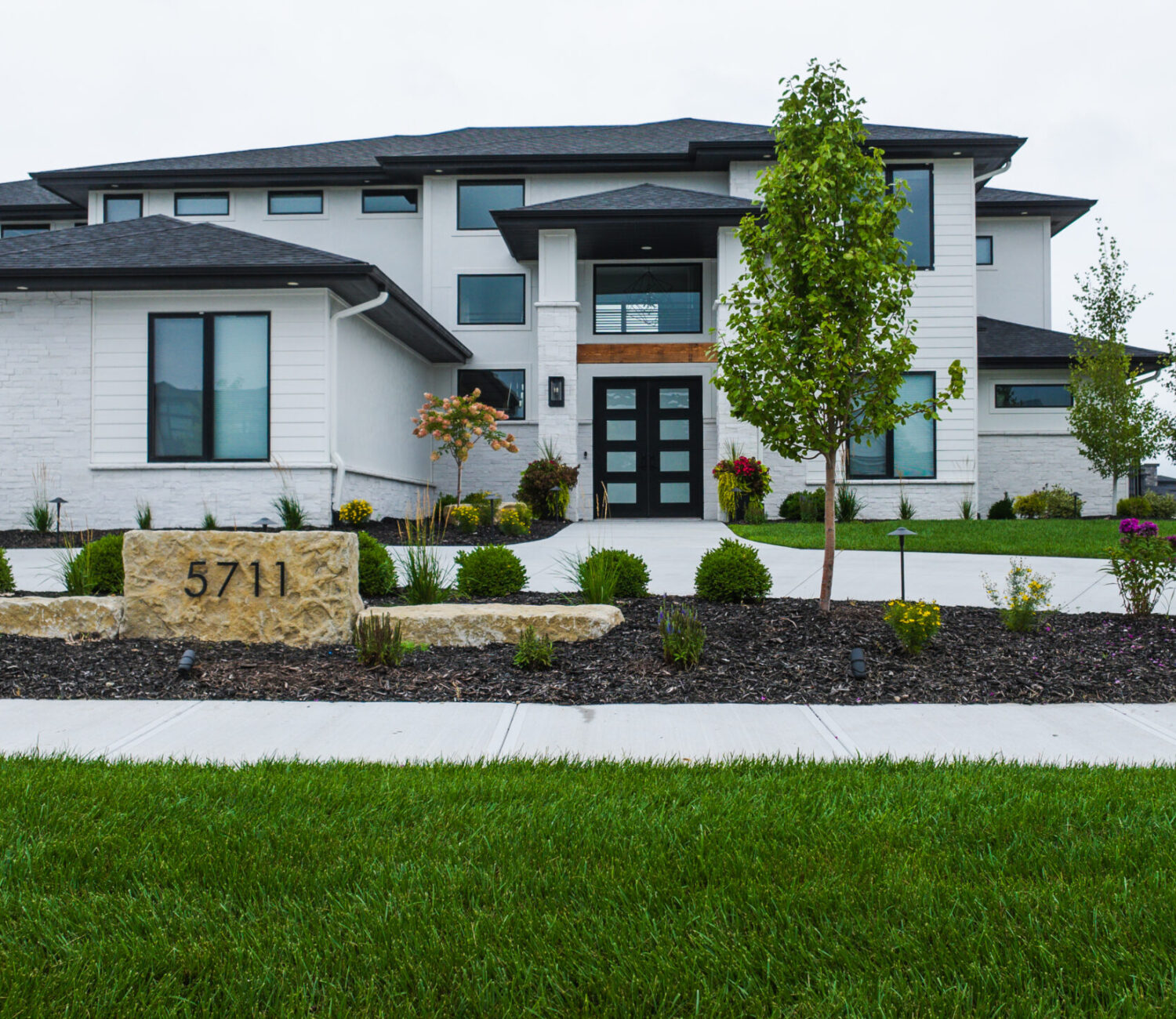 Modern home front yard landscaping with manicured lawn, dark mulch beds, and shrubbery