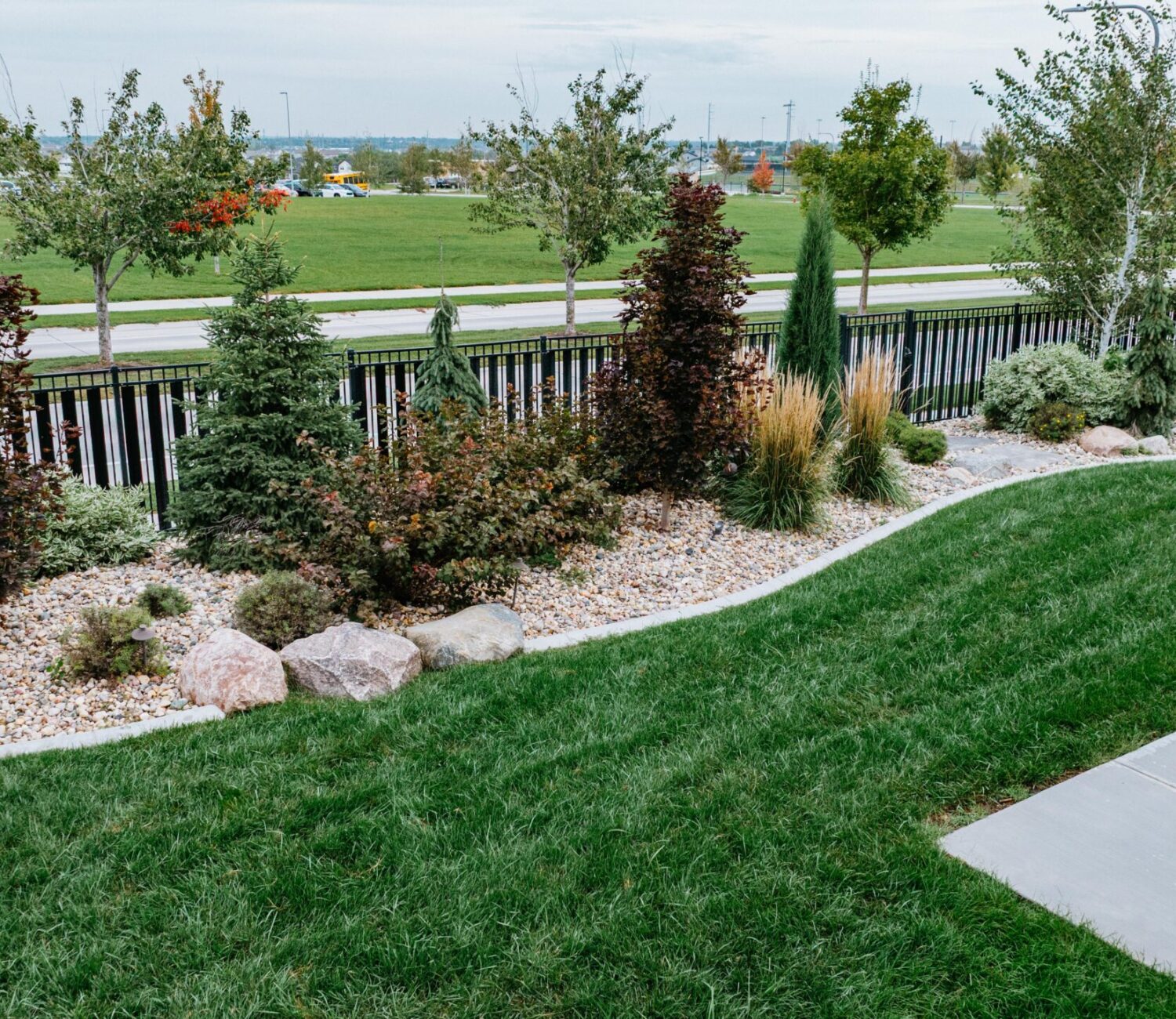 Residential landscape with green lawn, decorative rock beds, shrubs, and modern home exterior
