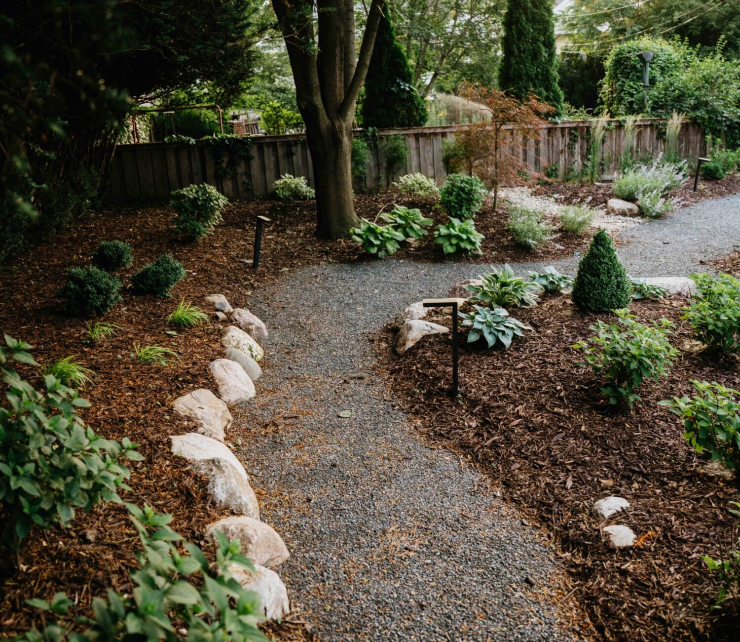 Crushed gravel garden path bordered by natural stone boulders and green foliage
