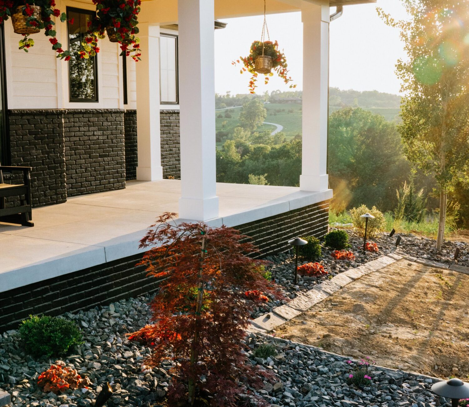 Covered front porch entry with dark river rock garden bed and decorative shrubs