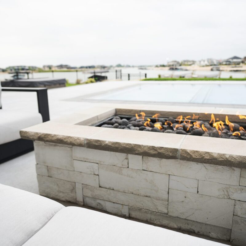Modern black gas fire bowl with active flames set on natural stone patio