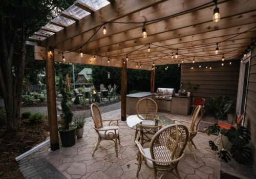 Custom wood pergola with string bistro lighting, patio seating, and built-in outdoor kitchen island