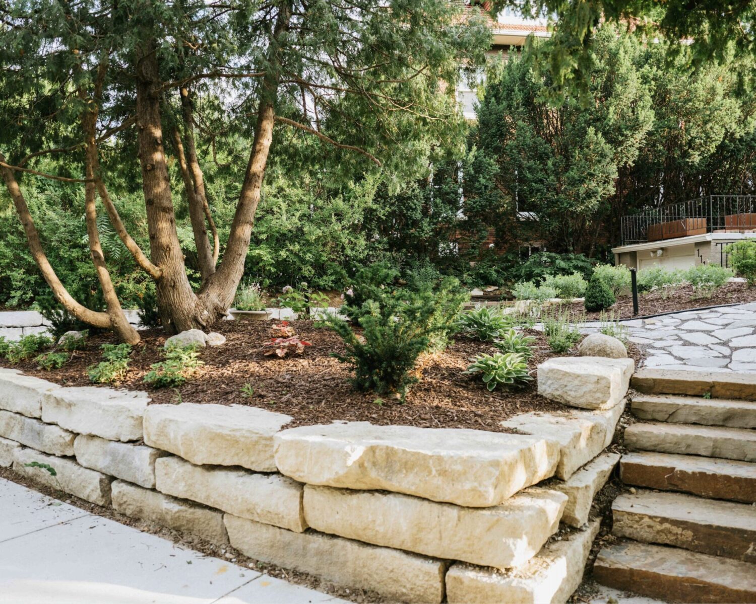 Stacked stone block retaining wall supporting terraced garden beds and lawn
