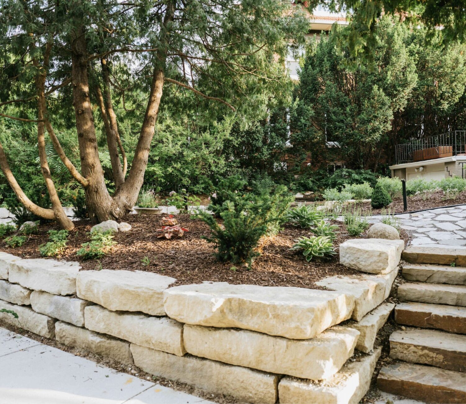 Stacked stone block retaining wall supporting terraced garden beds and lawn