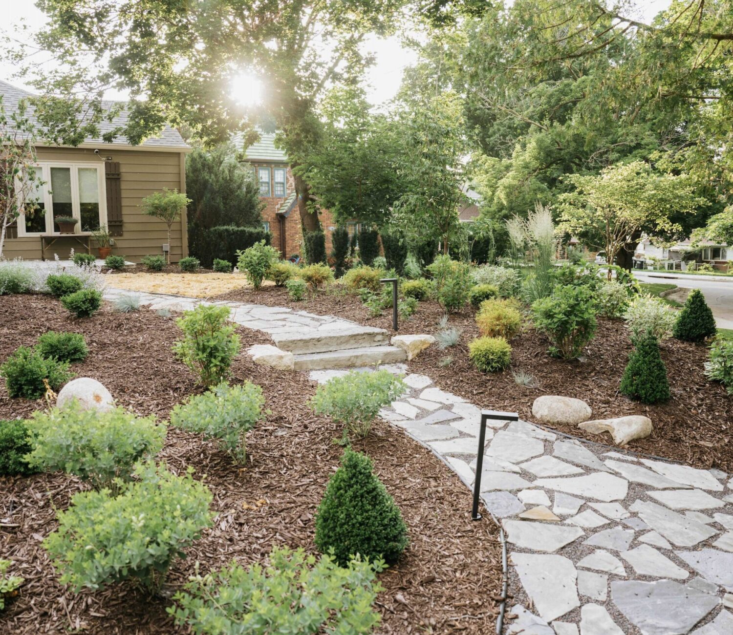 Flagstone stepping stone pathway winding through landscaped garden bed with mulch