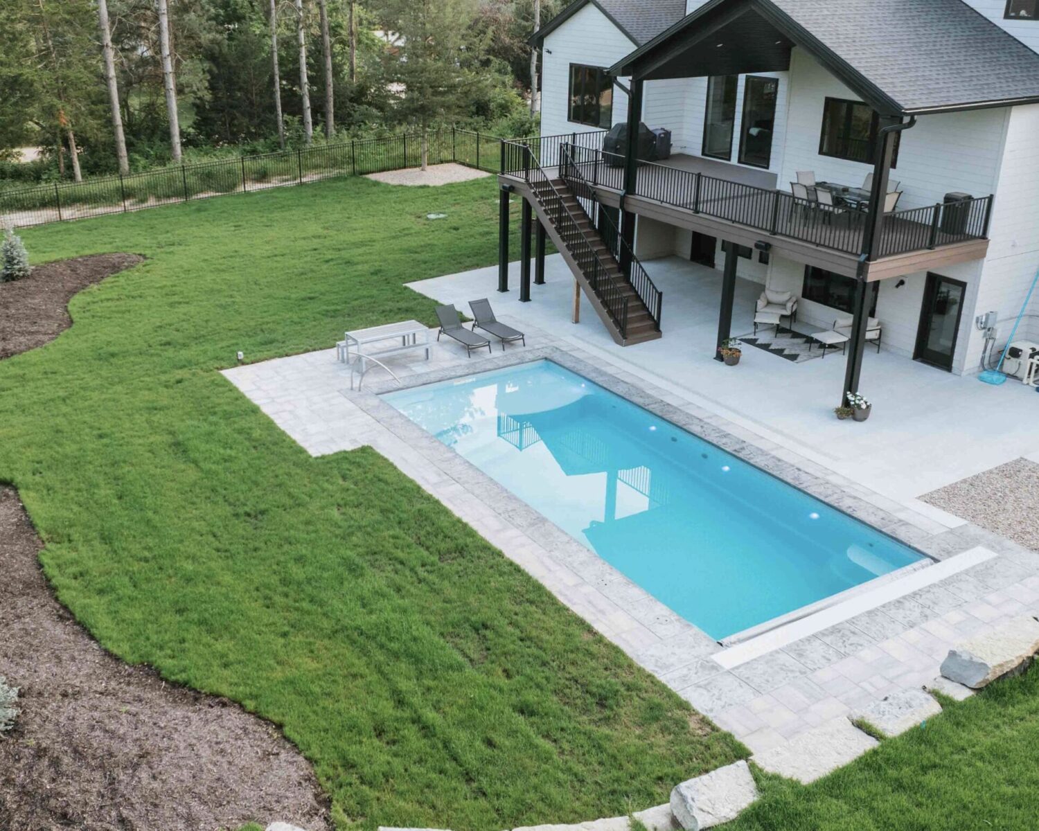 Backyard swimming pool surrounded by a spacious paver patio, manicured lawn, and covered outdoor living area.