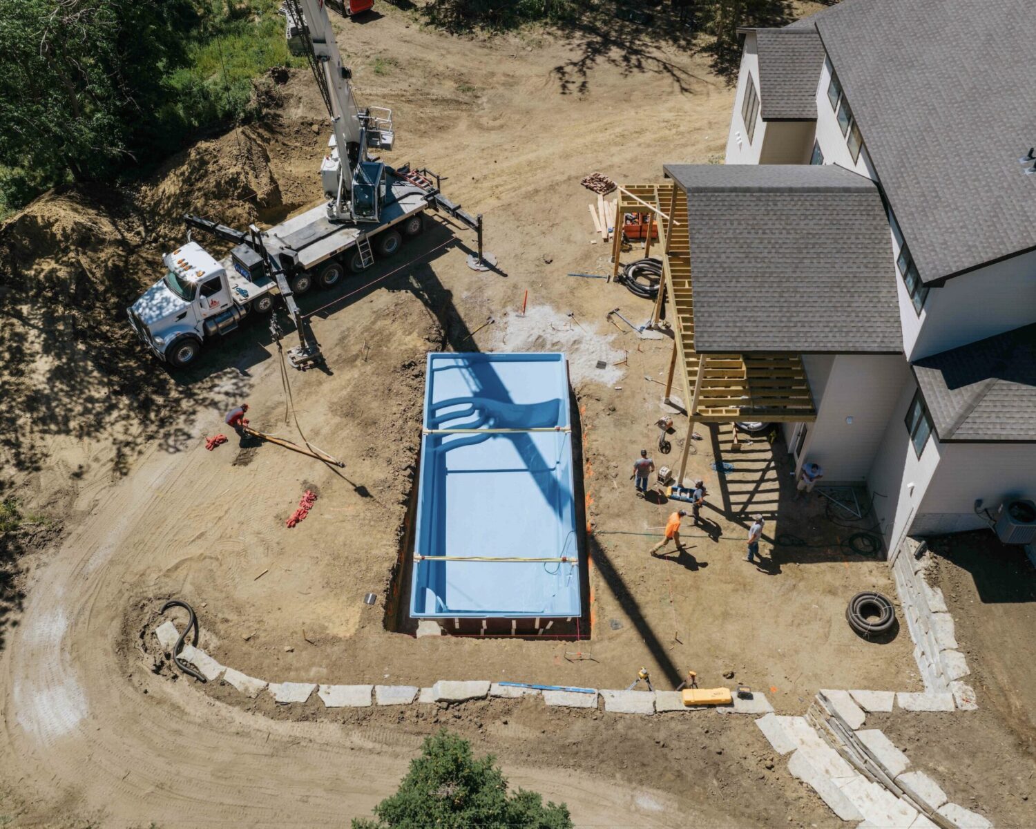 Under-construction backyard pool installation showing excavation work and crane placement