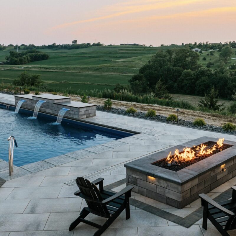 Poolside paver patio featuring custom stone fire pit table and adirondack lounge chairs