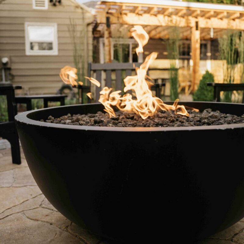 Modern outdoor fire pit surrounded by natural stone patio and landscaped backyard, creating a warm gathering space.