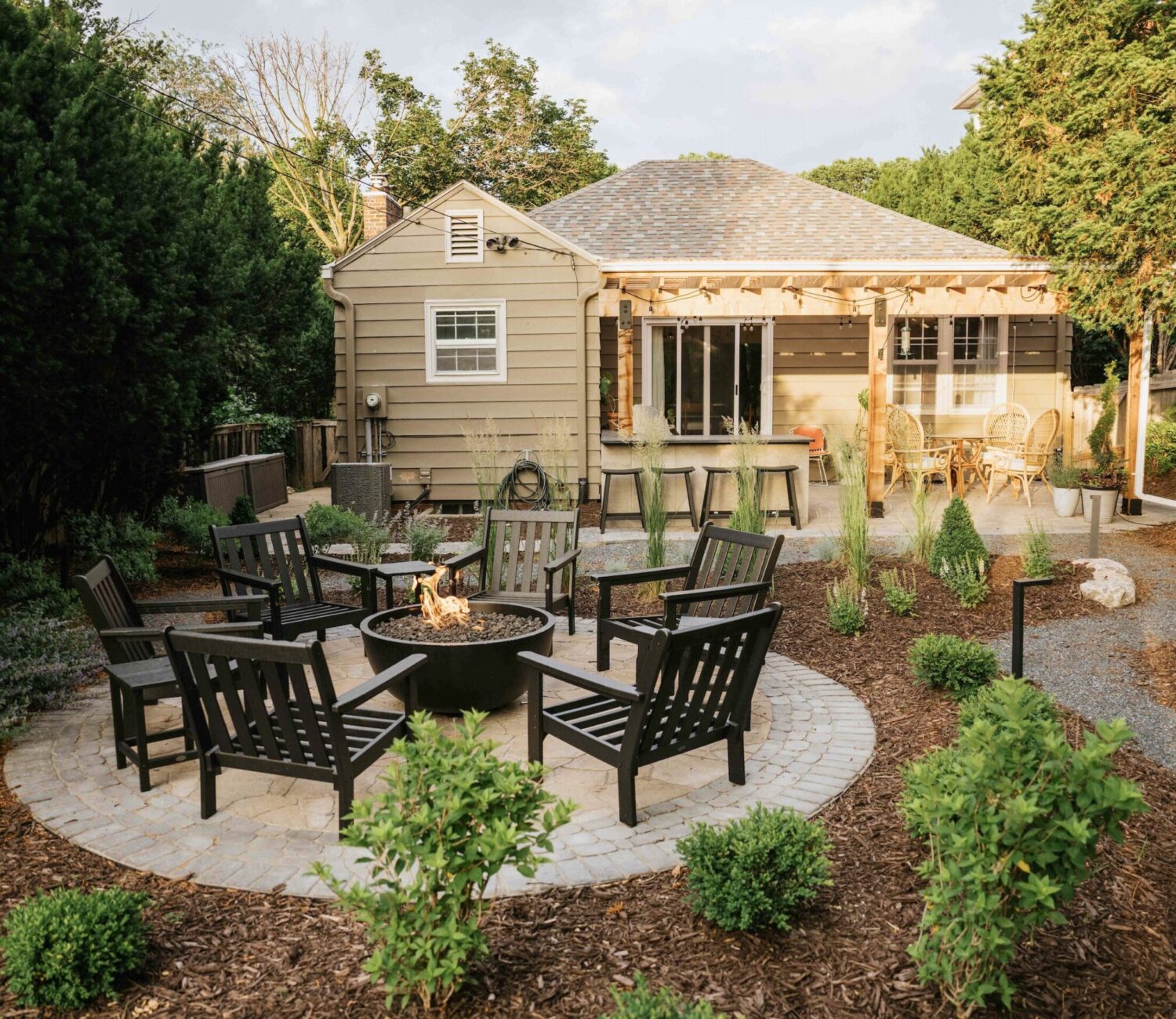 Patio fire pit lounge area set in mulched backyard garden surrounded by trees