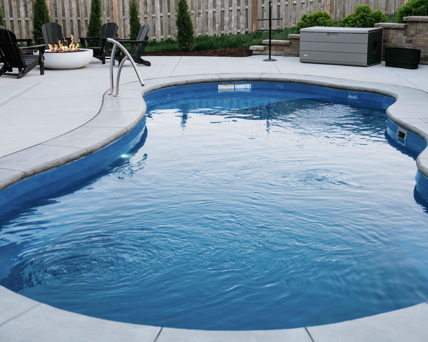 Curved inground pool with privacy tree landscaping, patio lounge chairs, and perimeter mulch beds