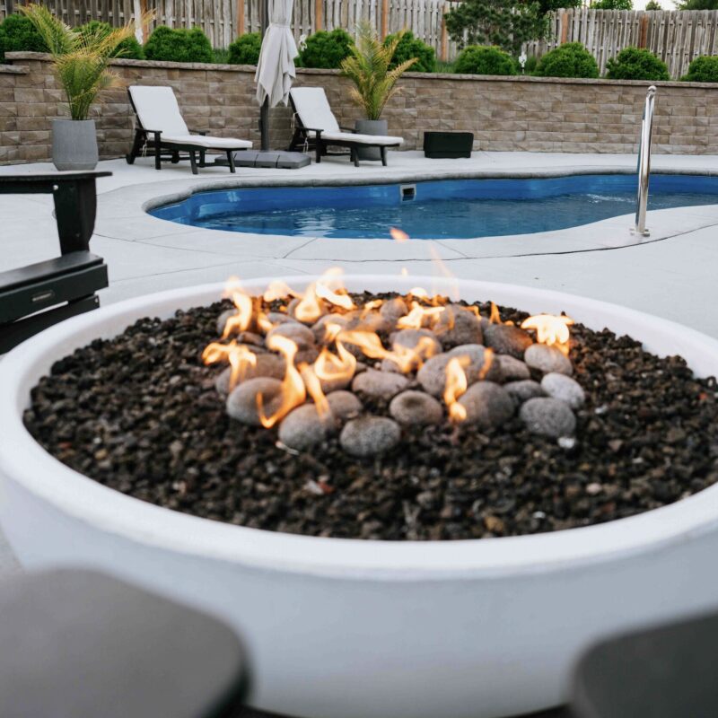Round gas fire bowl with lava rock set on concrete pool patio deck