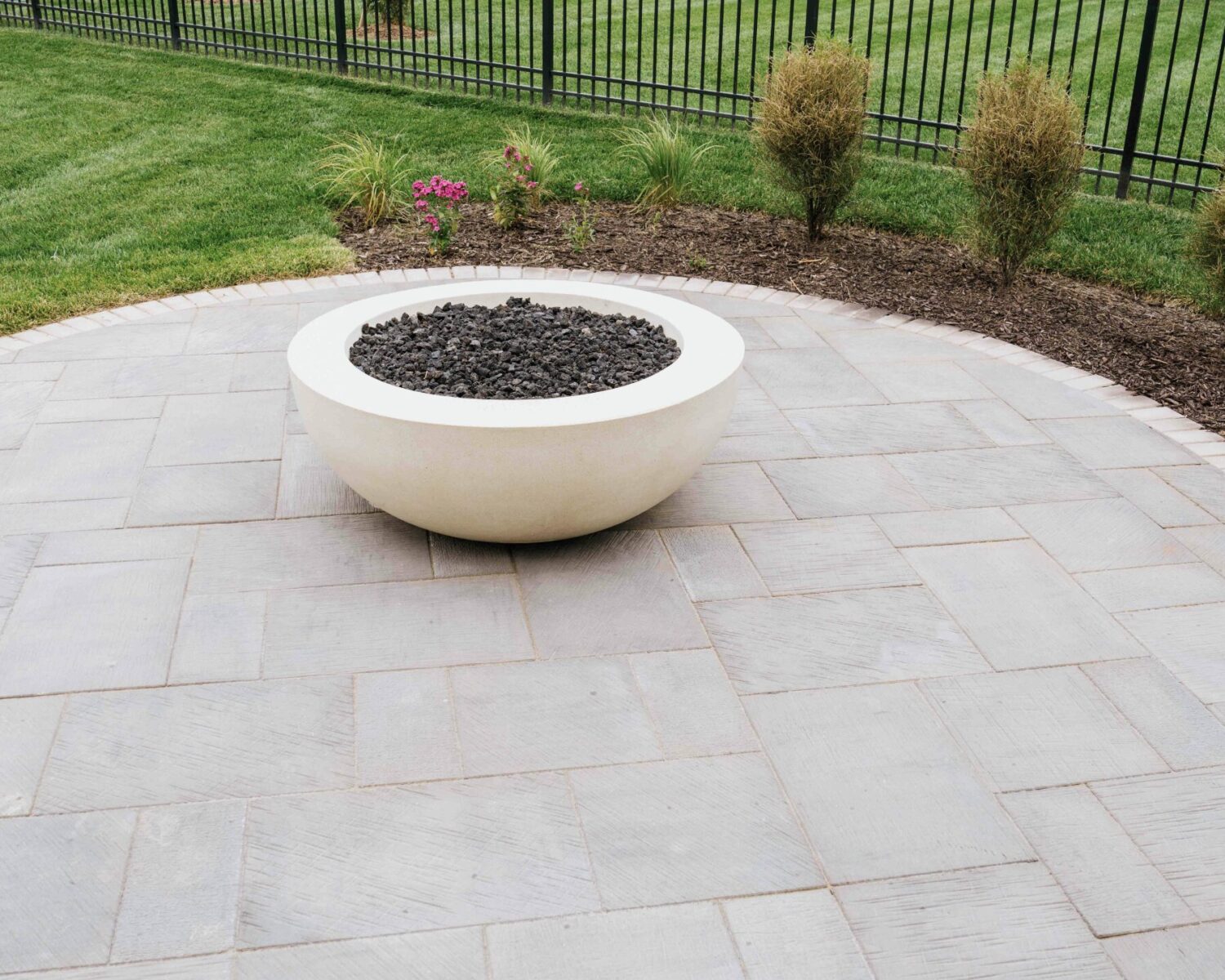 Round white gas fire bowl installed on concrete paver patio surrounded by green lawn