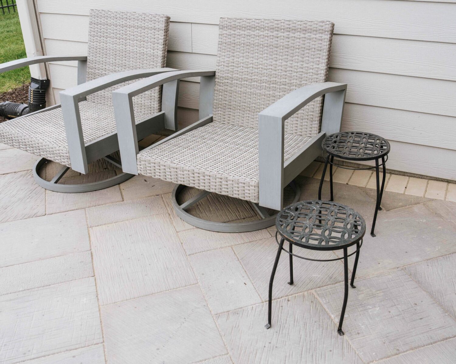 Outdoor patio lounge chairs with metal side tables set against neutral home siding