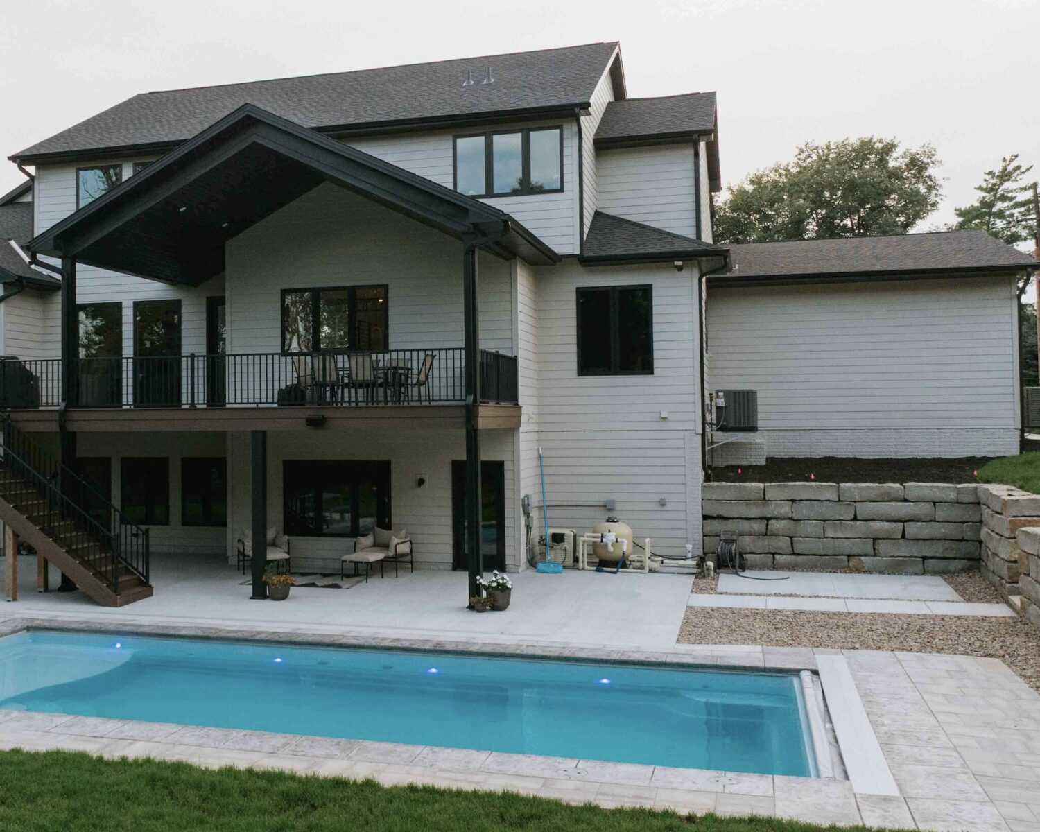Rectangular inground swimming pool set behind a two-story modern home with custom stone patio