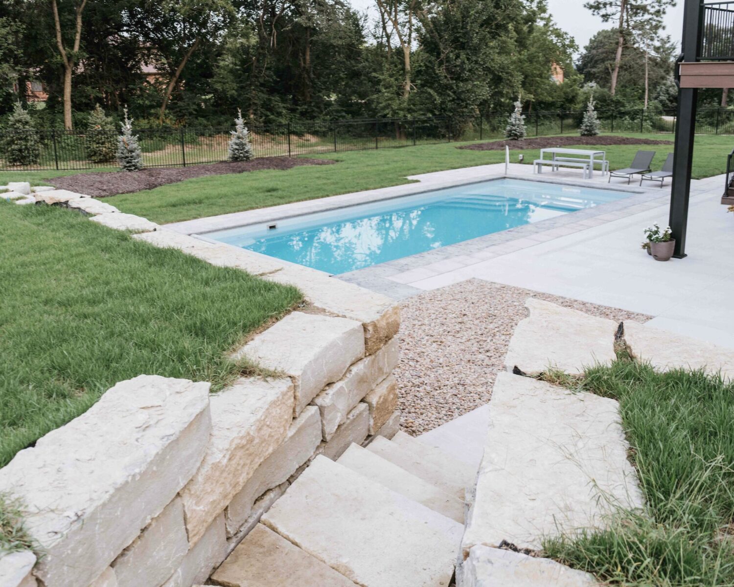 Multi-tiered stone block retaining wall with stairs leading to a backyard inground swimming pool