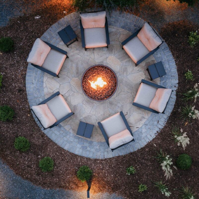 Overhead view of circular paver patio fire pit with white armchairs and landscape lighting
