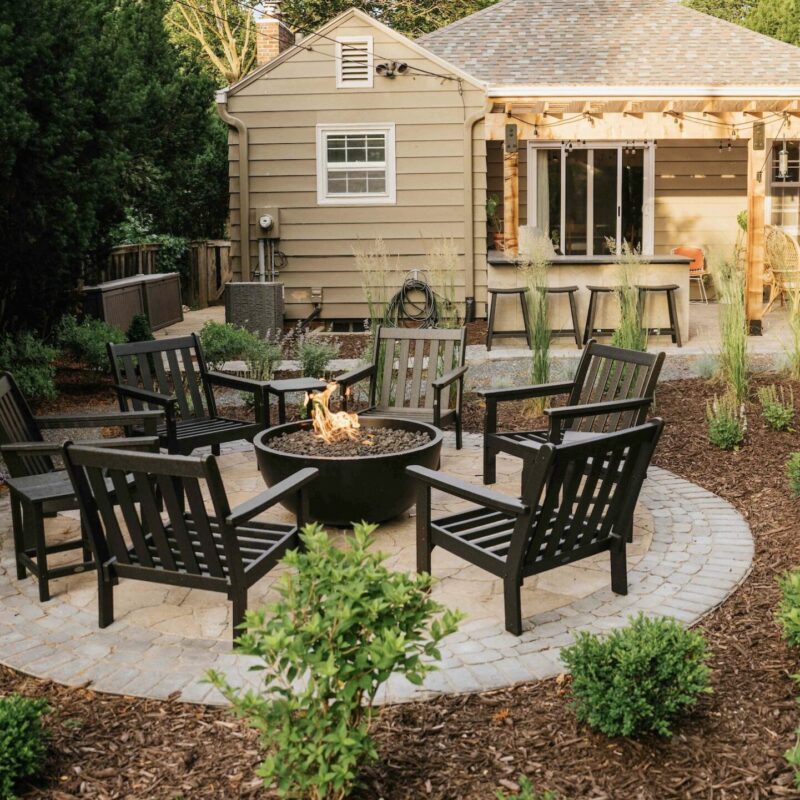 Patio fire pit seating area with wooden pergola and surrounding landscape design