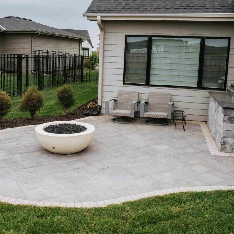 Small white gas fire bowl on custom paver patio exterior of modern home
