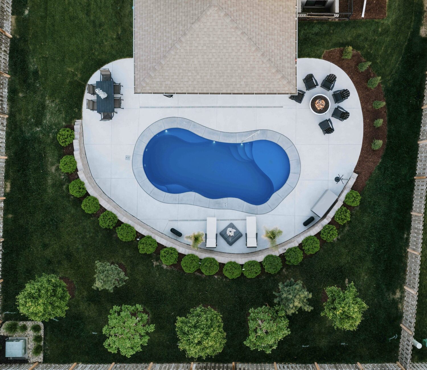 Top-down view of a custom freeform inground pool framed by lush garden beds and trees