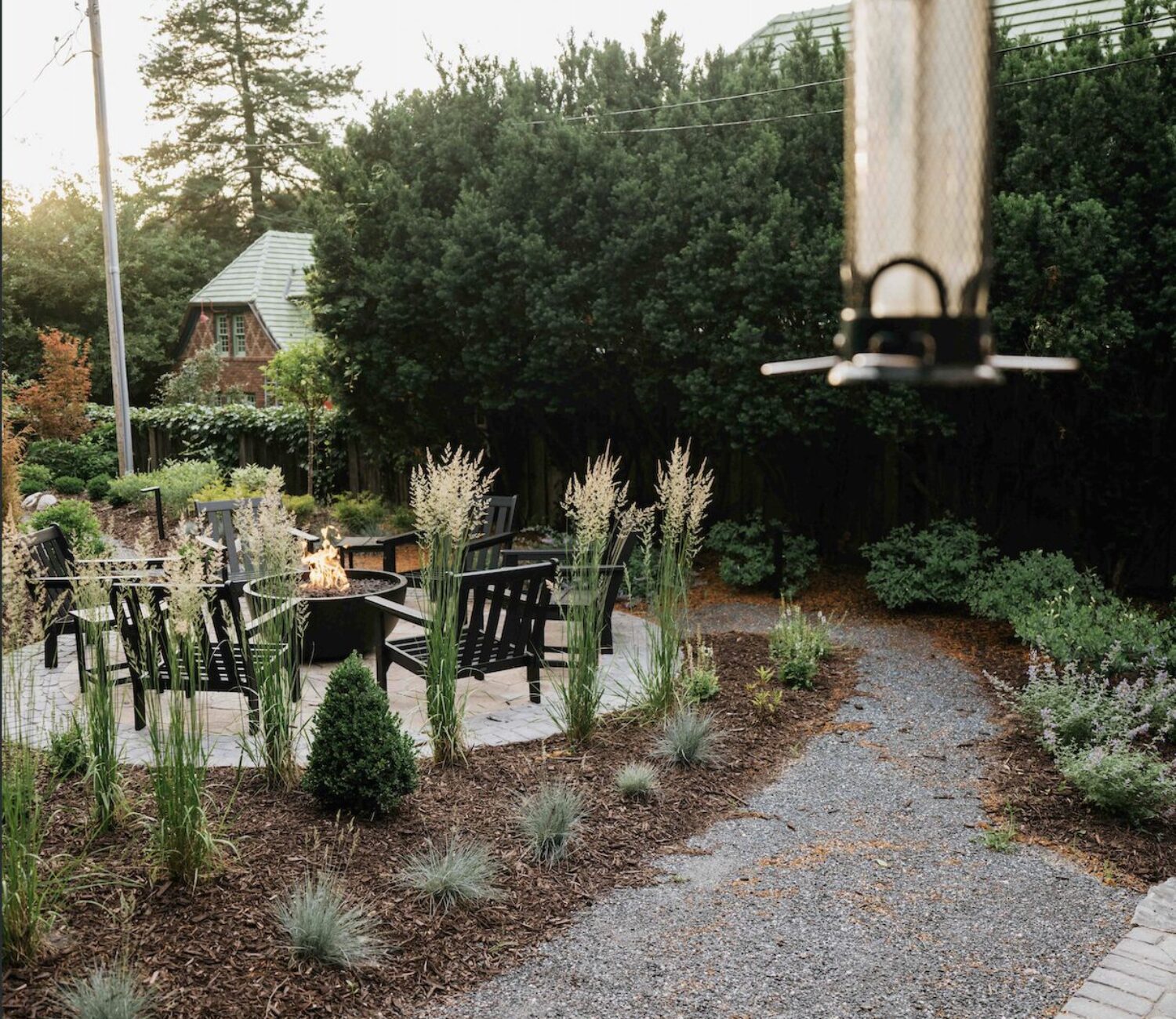 Gravel garden walkway leading through shady backyard landscape with bird feeder
