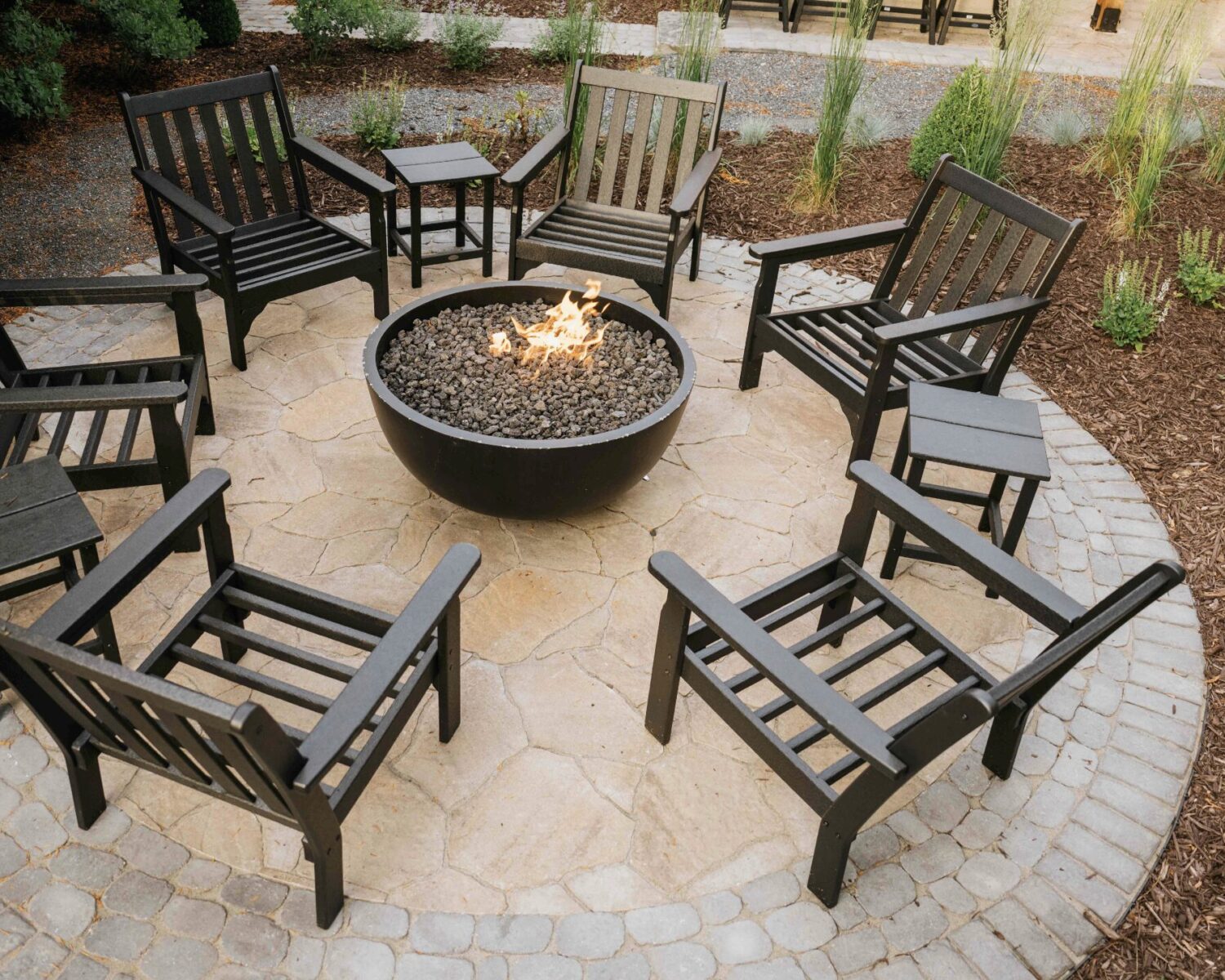 Top-down view of round gas fire pit table with dark adirondack chair seating on stone patio